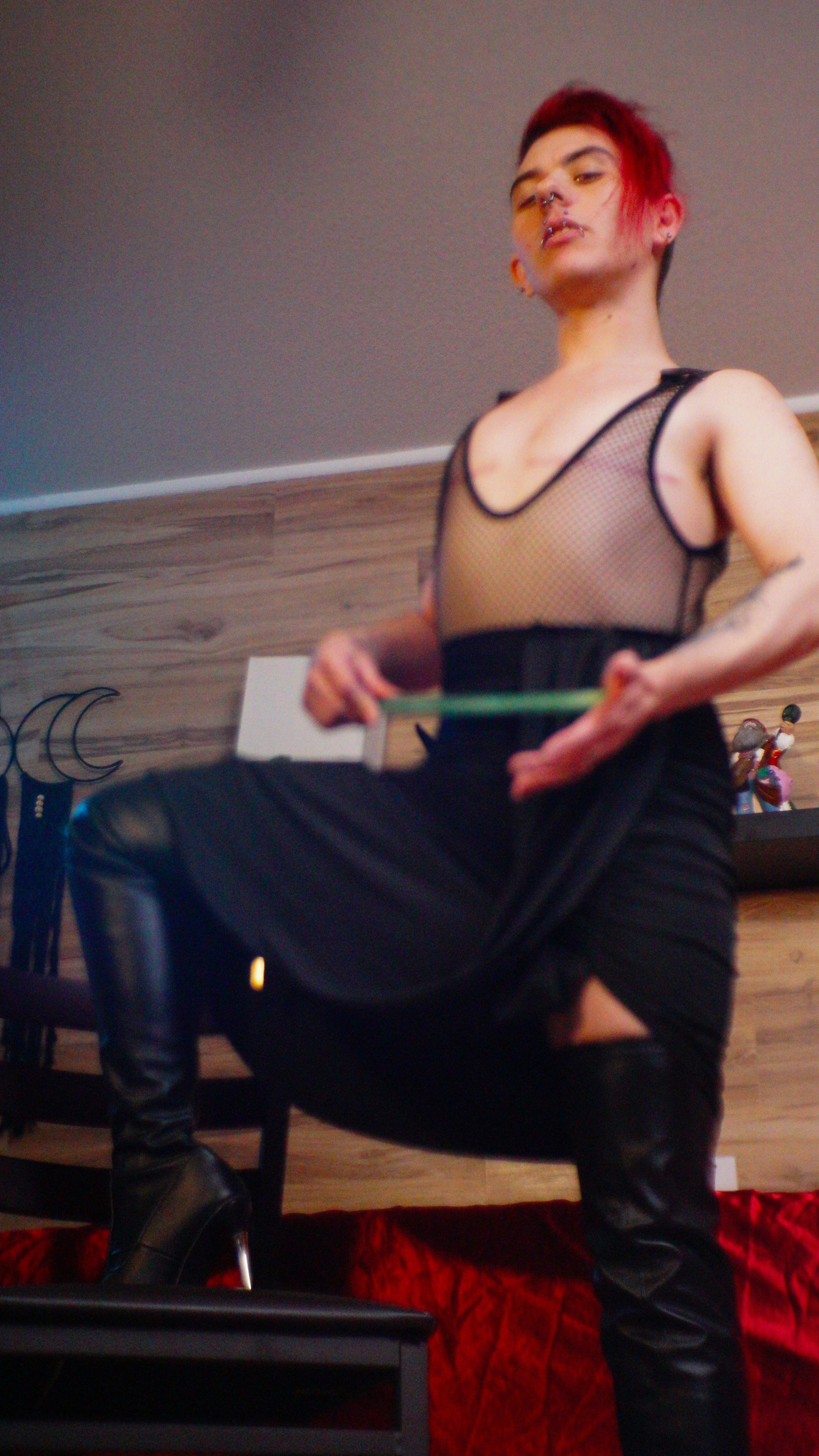 Standing tall, one foot on a chair, slapping a paint stick on his hand.