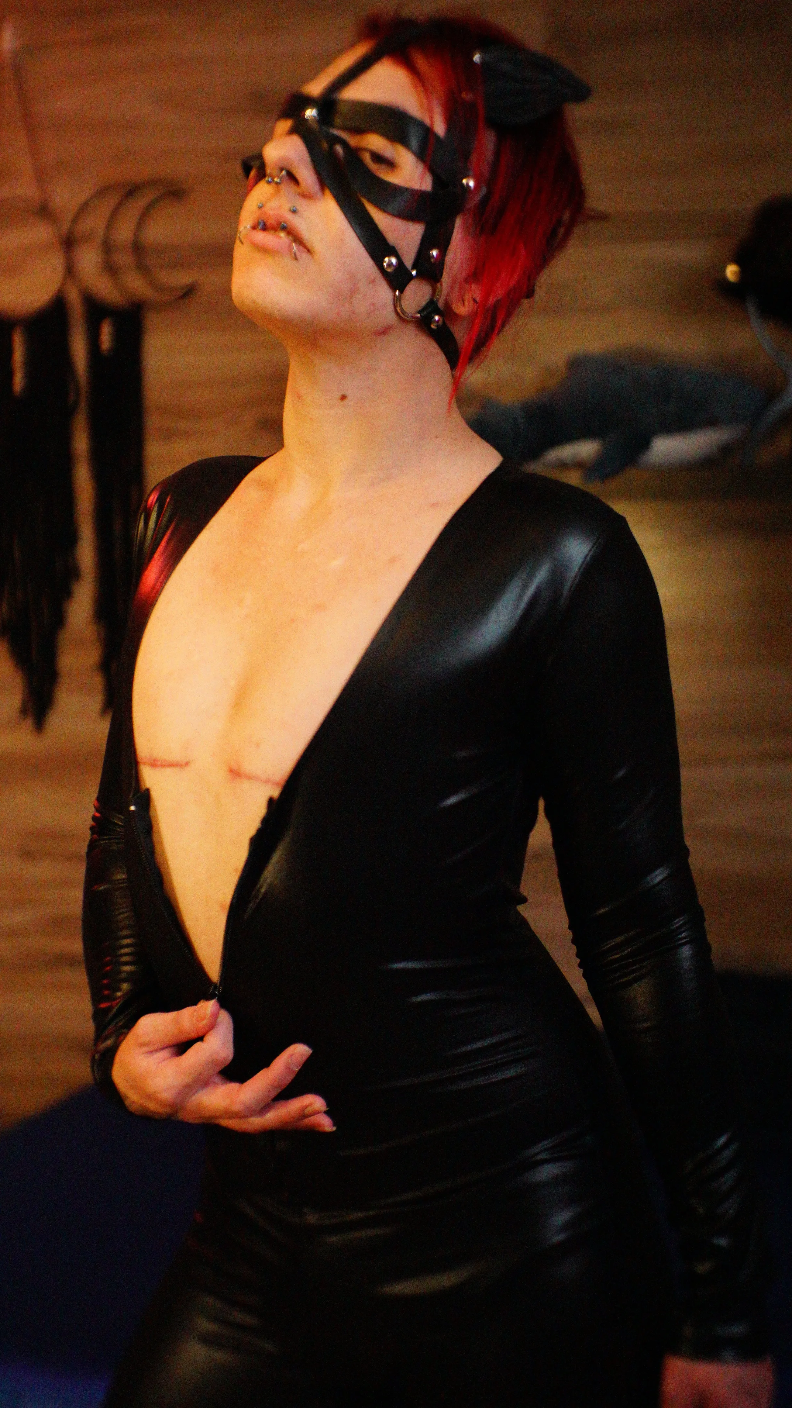 Kane wearing a black catsuit and cat-eye mask; the front zipper being pulled half-way down