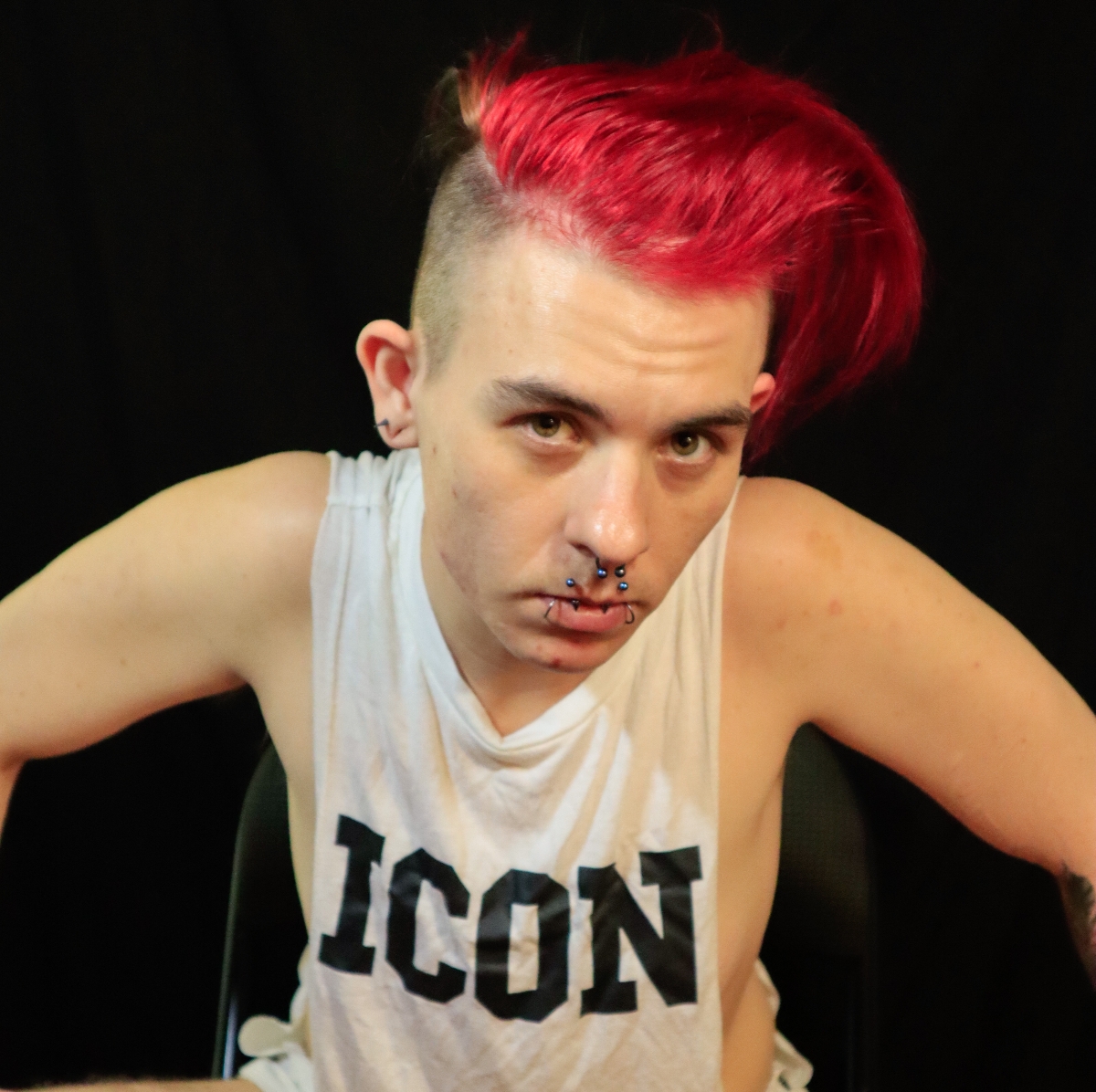 Sitting forward on a chair, wearing a shirt that says Icon